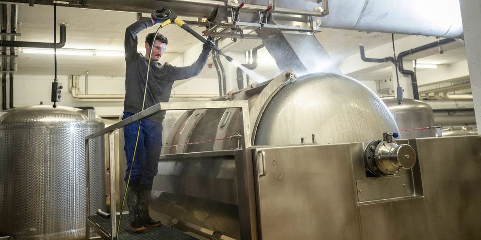 A man cleans a wine grape press with a Kärcher high-pressure cleaner