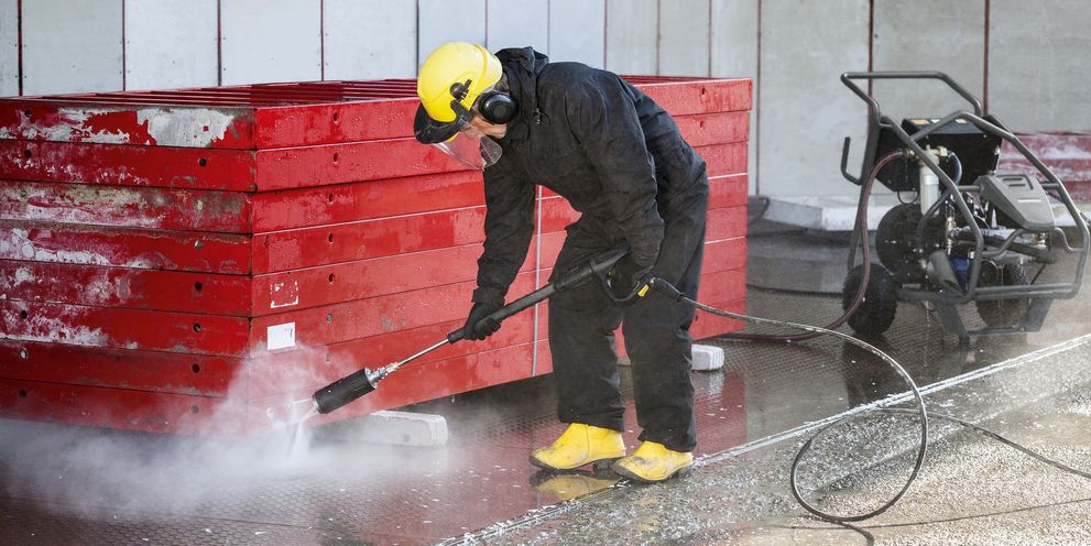 A person in protective clothing and a helmet cleans shuttering using a Kärcher Ultra-High-Pressure Cleaner