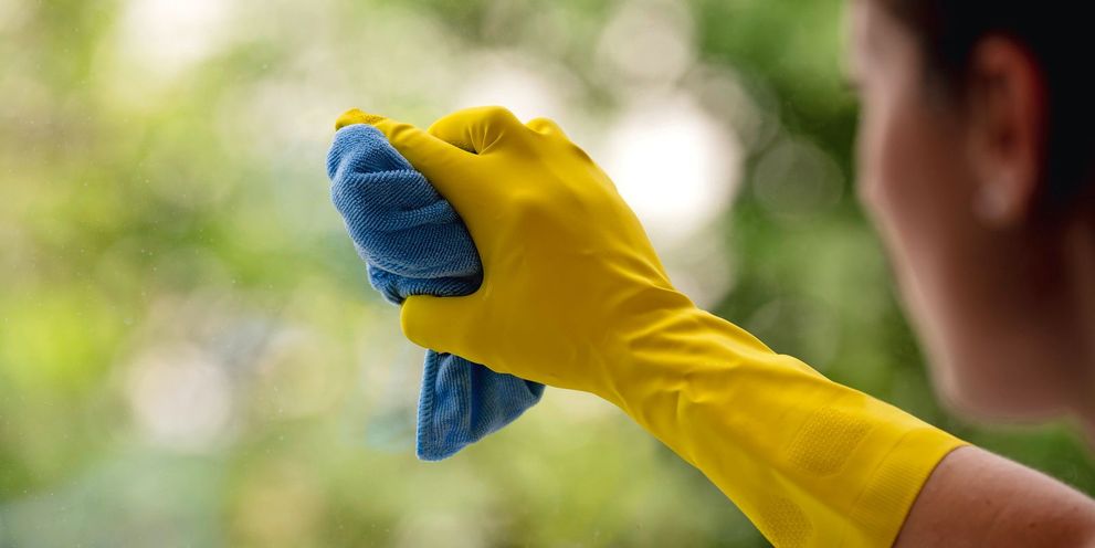 A woman cleans a windshield using a glove and cloth
