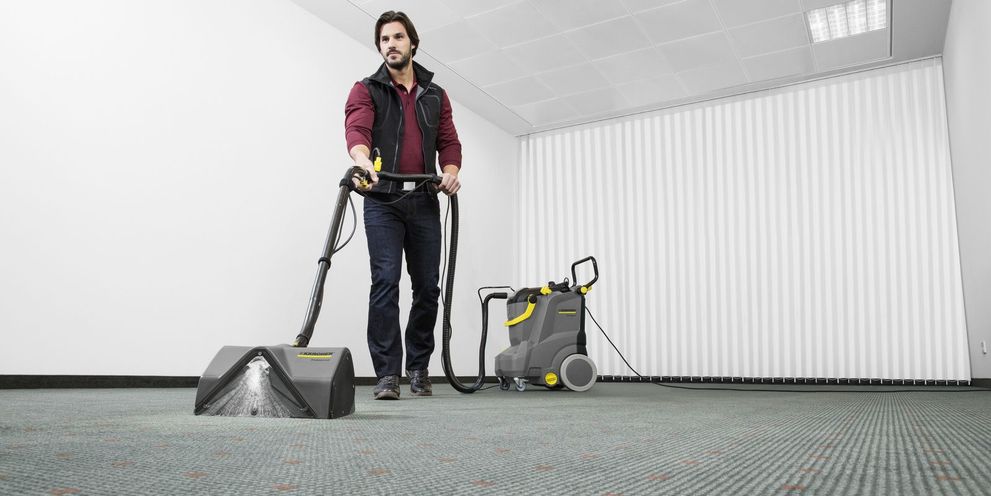 Carpet cleaning with spray extraction A man cleaning a very large carpet in a room with a Kärcher spray-extraction cleaner