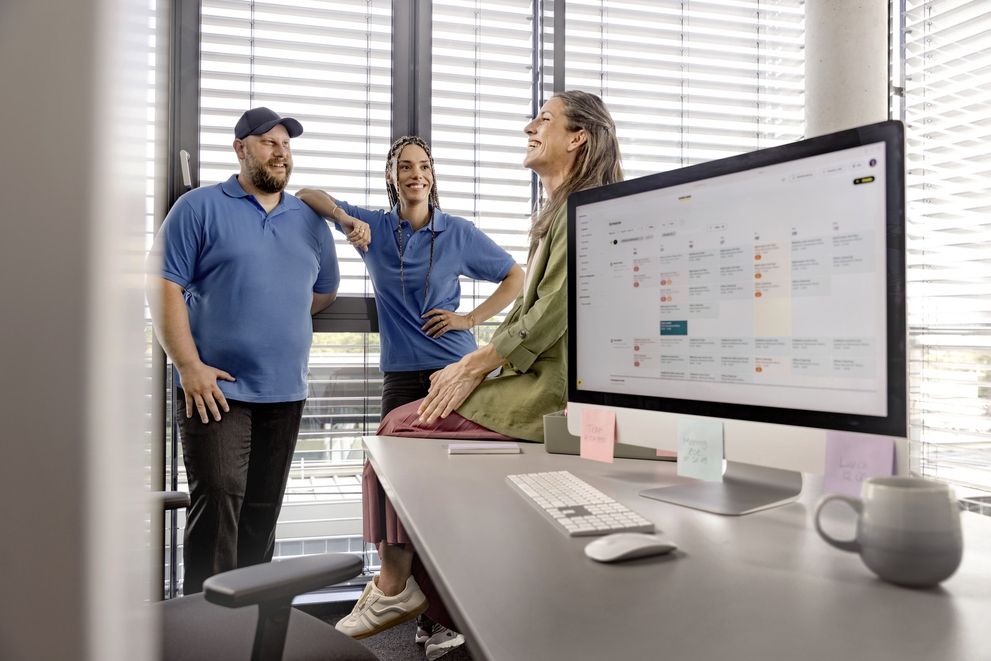 Persons standing around an office computer with a work schedule