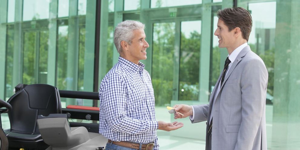 The foundation for good financing is the trust between both contract partners – this is true in the cleaning industry, too. A person in a suit hands another person a key for a Kärcher sweeper machine