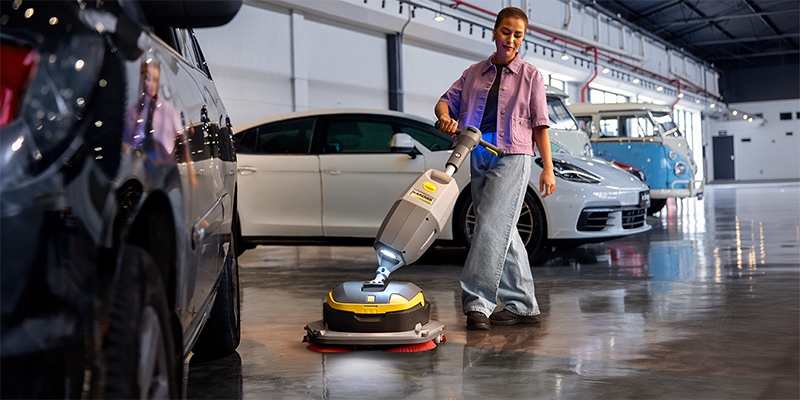 Vrouw die de vloer aan het schrobben is in een showroom met auto's