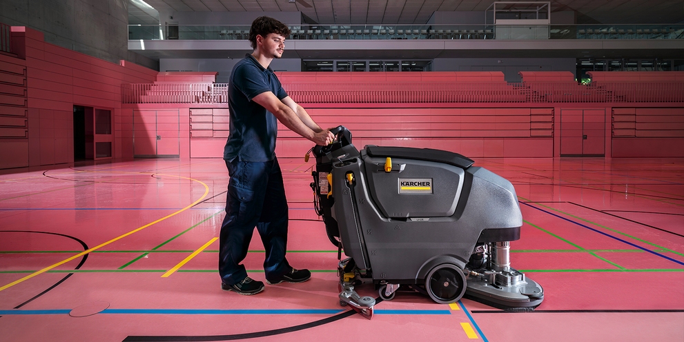 man in gymzaal met een schrob-/zuigmachine
