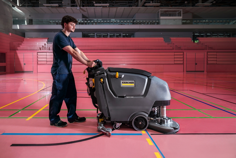 man achter een schrobmachine door een sporthal 