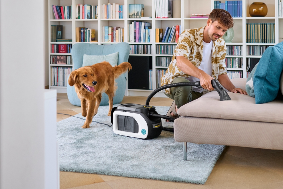 hond die naast een man staat die de bank aan het schoonmaken is met een tapijtreinger