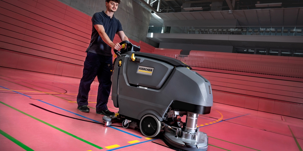 man achter schrobmachine in een sporthal 
