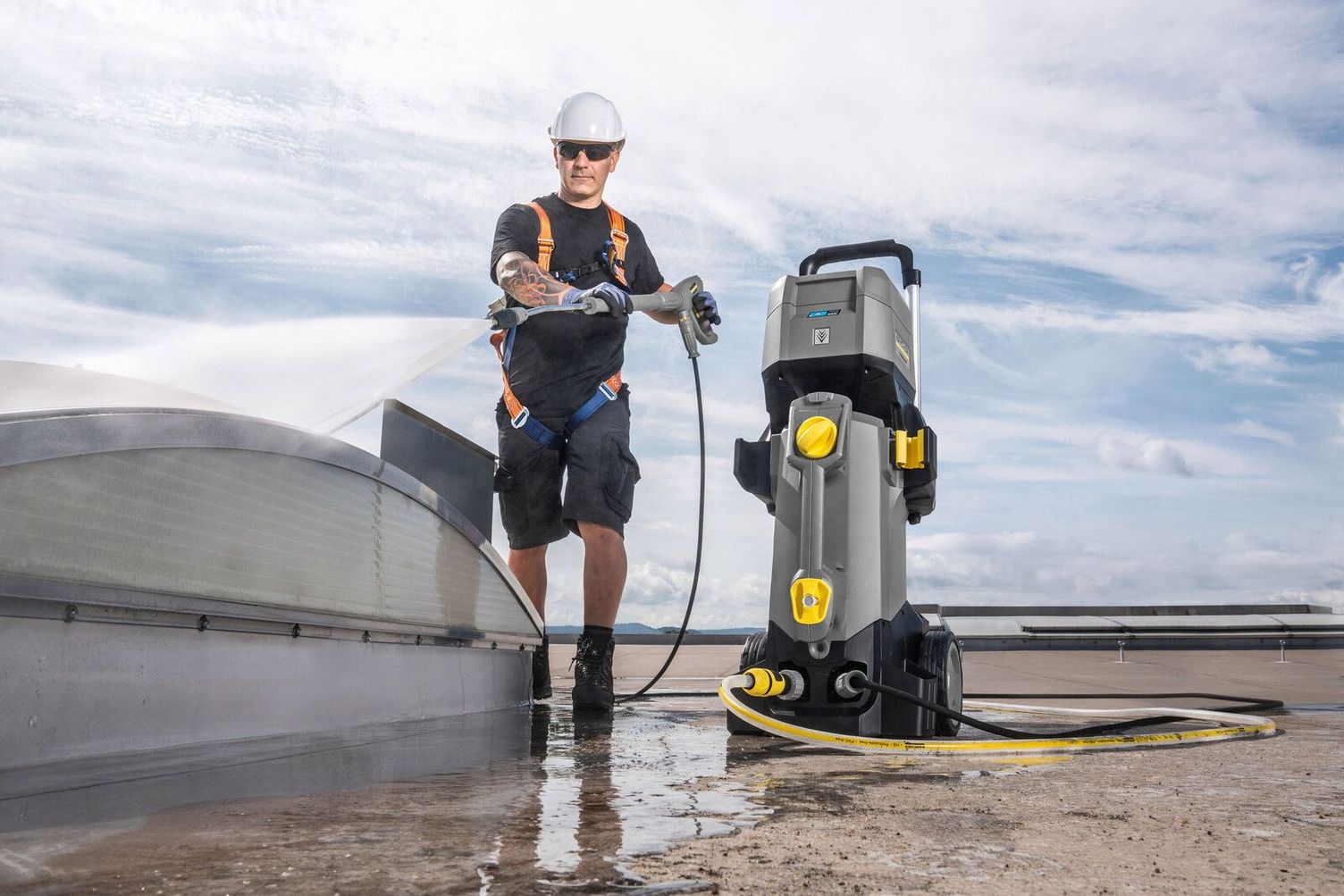A person wearing a helmet cleans a roof with the help of a Kärcher Battery Powered High-Pressure Cleaner