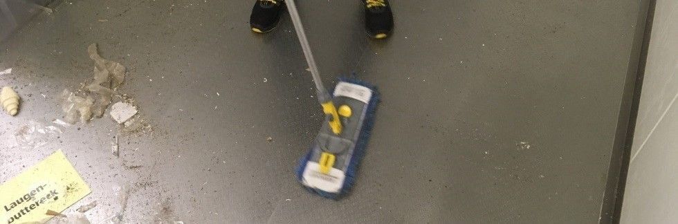 View of a dirty floor with dust and pieces of paper. One person holds a mop in his hand and cleans the floor.