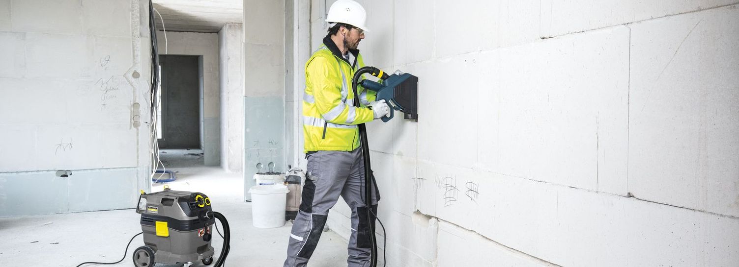 A person in protective clothing cleans a wall in the shell with a safety vacuum cleaner.