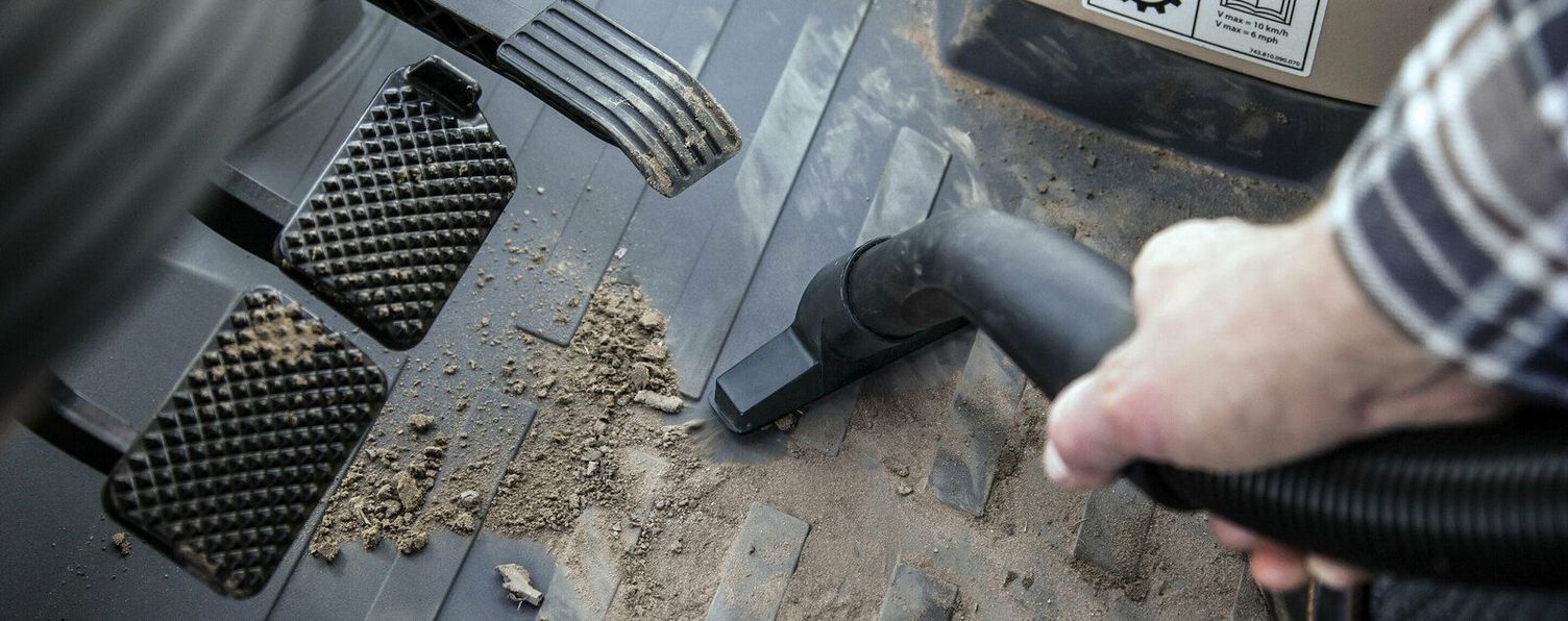 One hand uses a Kärcher Vacuum Cleaner to clean the inside of the cab