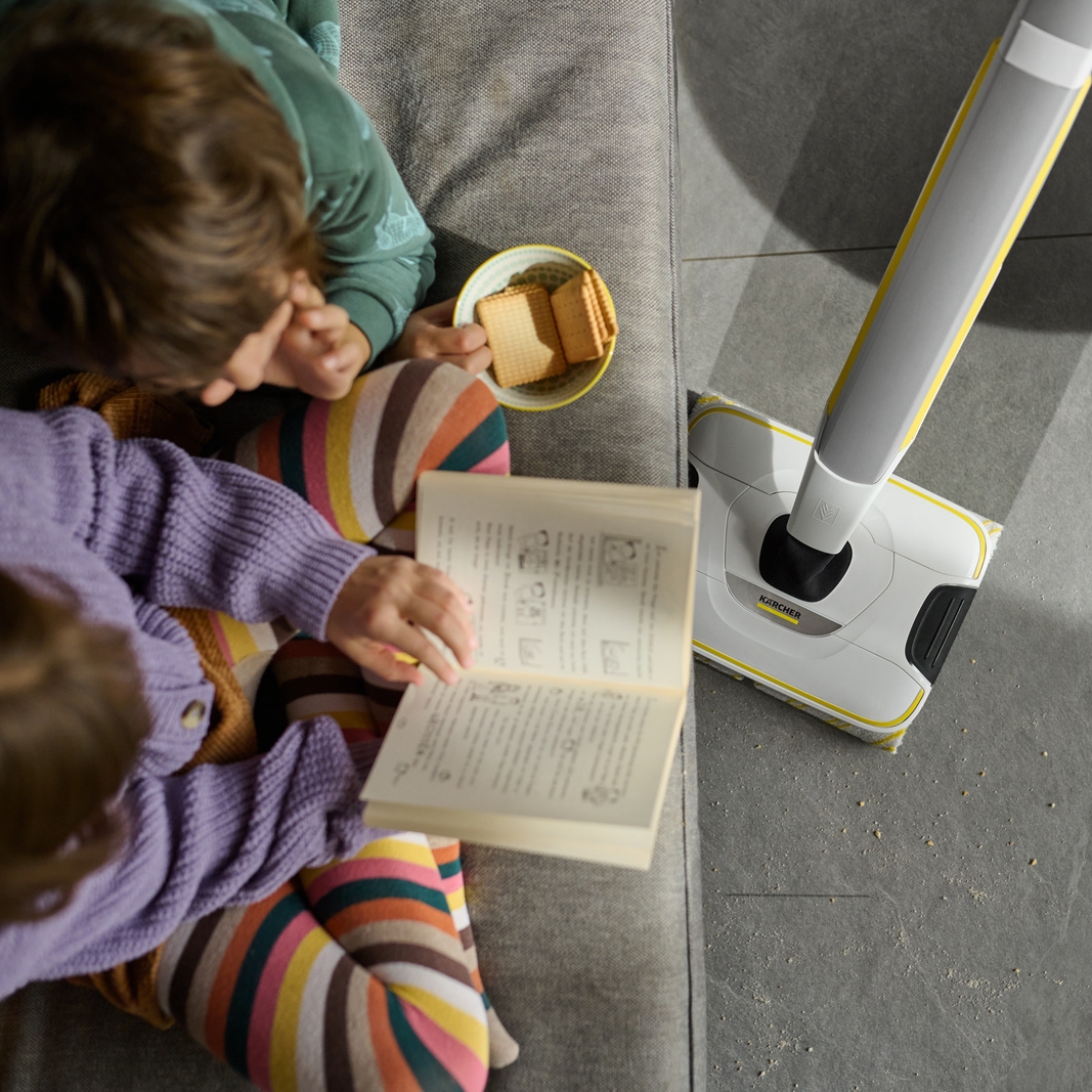 Silent floor cleaner cleaning tiles next to children reading Silent floor cleaner cleaning tiles next to children reading
