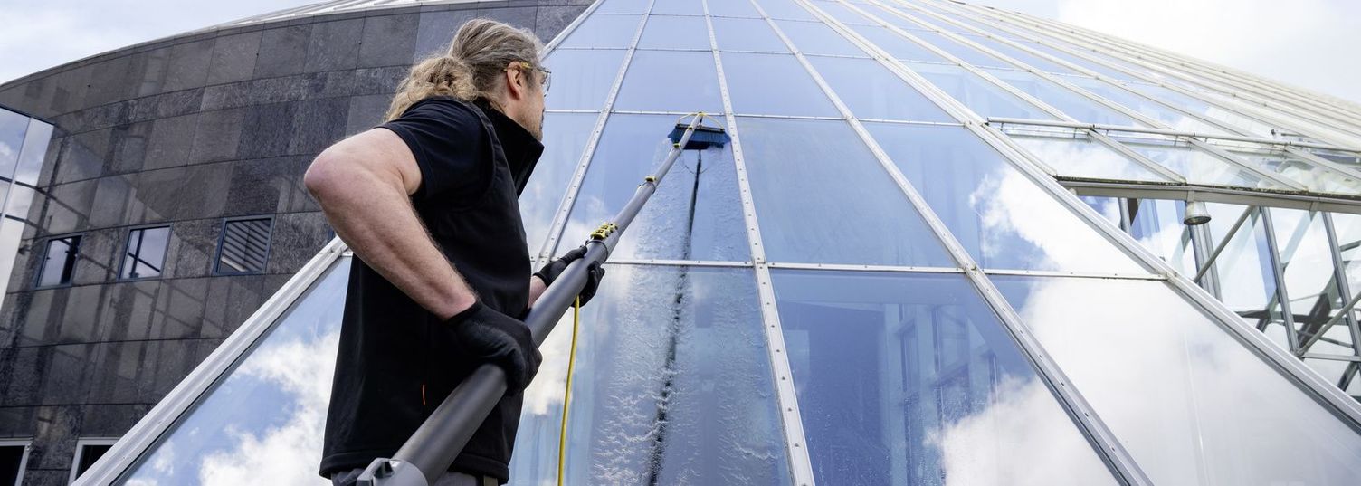 Commercial window cleaning A person cleans a slanted glass facade with the help of a water-fed pole