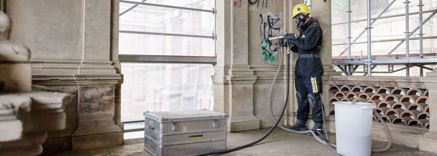 A person in protective clothing removes graffiti from the inside of a house wall