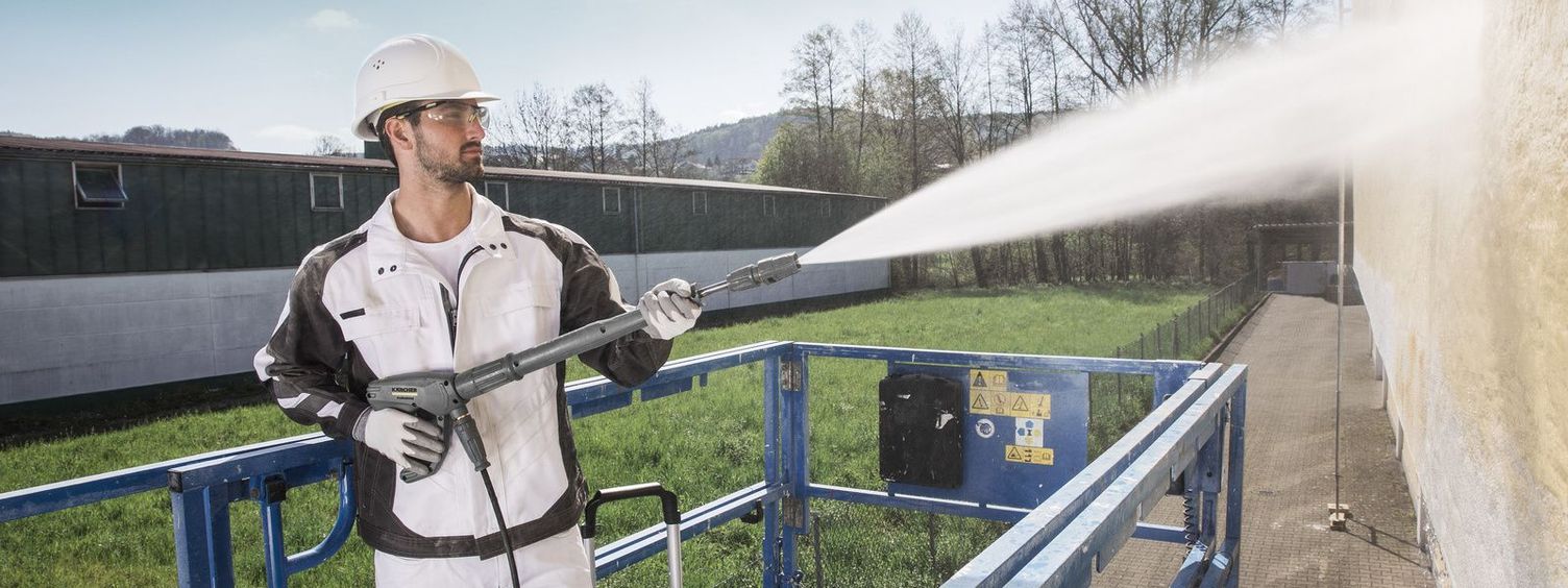 A person on a hoist uses a Kärcher High-Pressure Cleaner for facade cleaning