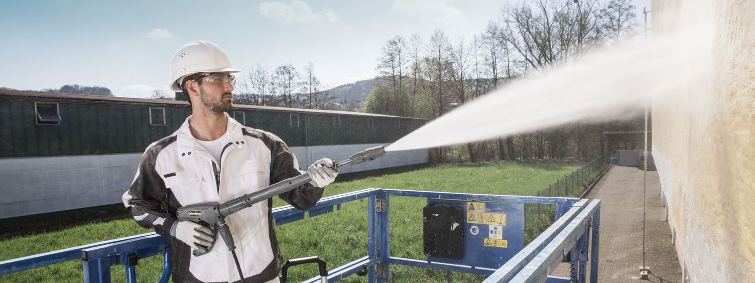 A person on a hoist uses a Kärcher High-Pressure Cleaner for facade cleaning