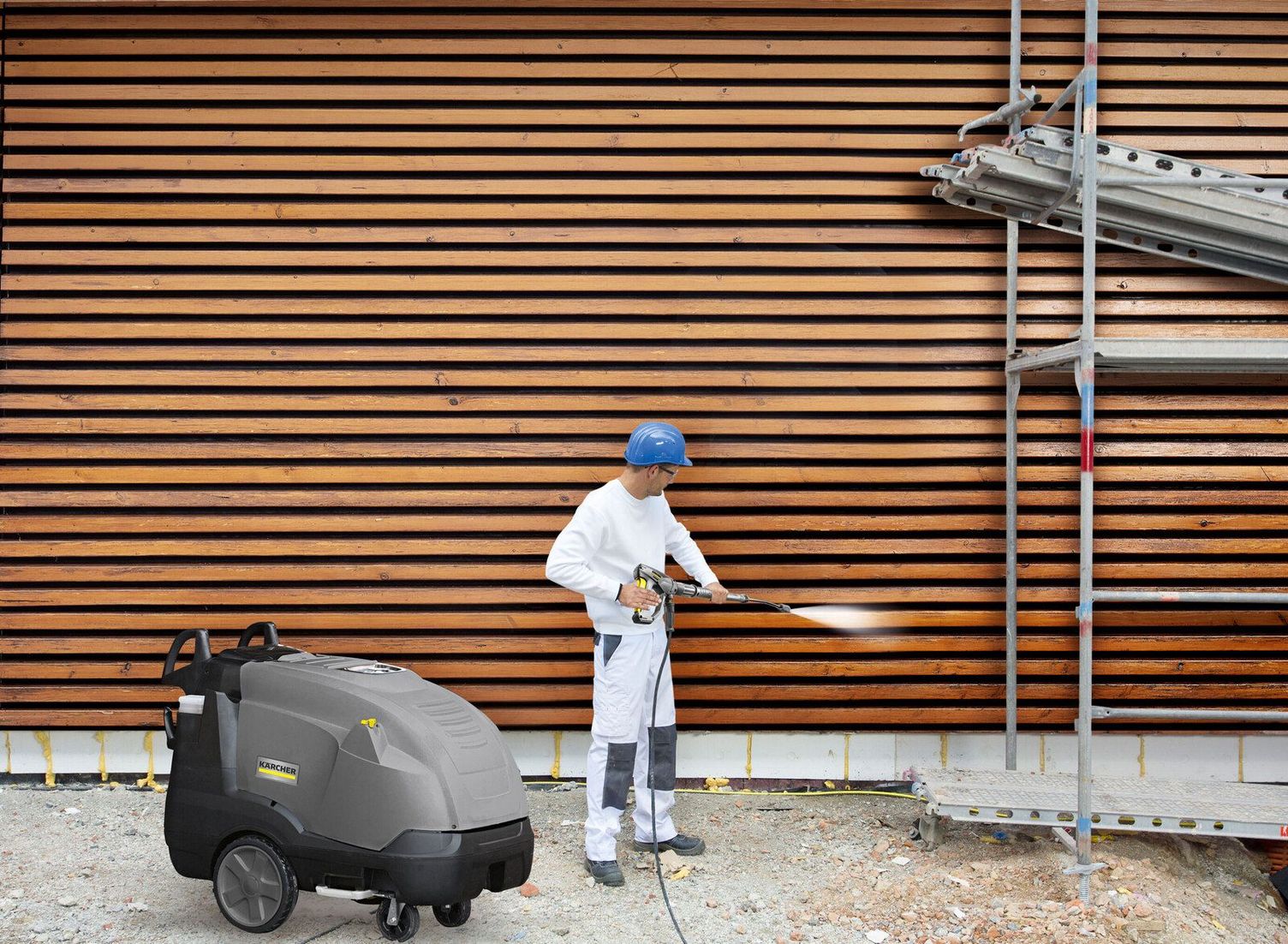 Cleaning wooden facades with hot water high-pressure cleaners A person in work clothes uses a Kärcher HDS Trailer to clean a wooden facade