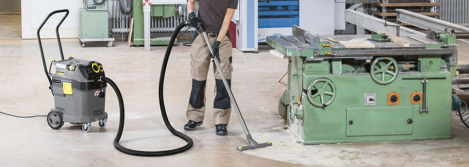 A person cleans the floor in a workshop using a Kärcher Vacuum Cleaner