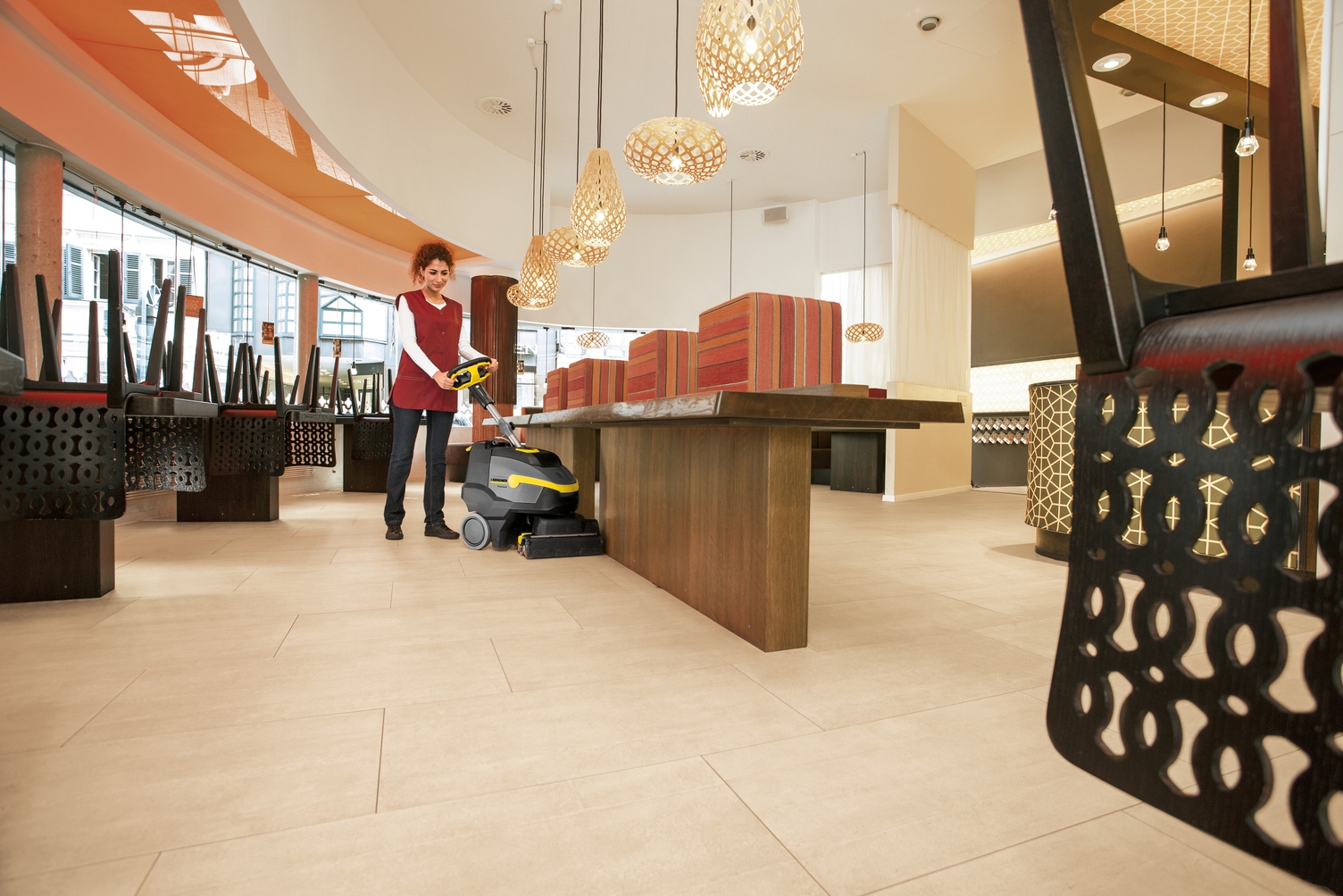 A person cleaning a dining area with a Kärcher scrubber dryer.