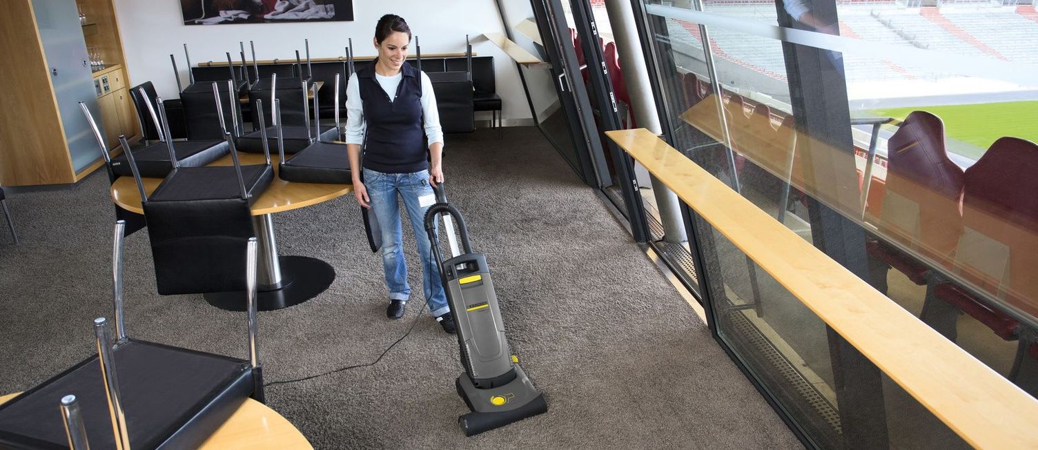 A woman cleaning the box in a stadium with a Kärcher upright carpet vacuum