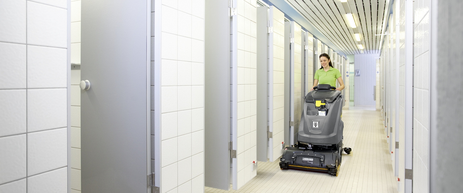 A person cleans the tiled floor with a scrubber-dryer from Kärcher.