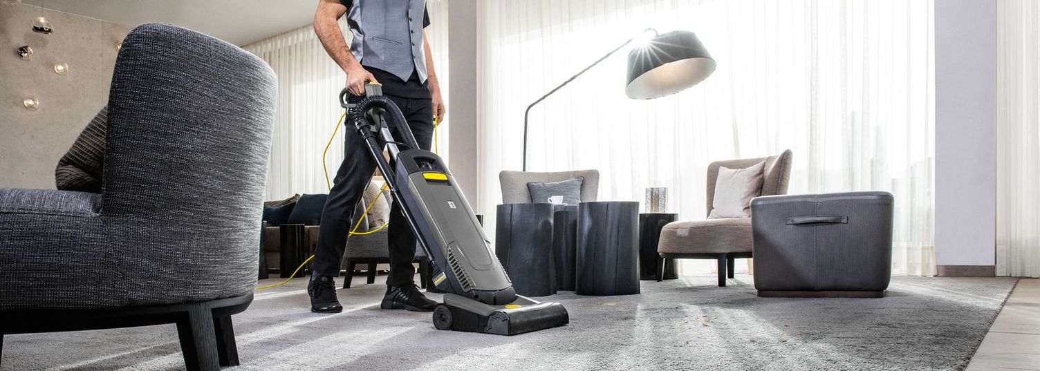 A man cleans the carpet in a hotel room with a Kärcher device