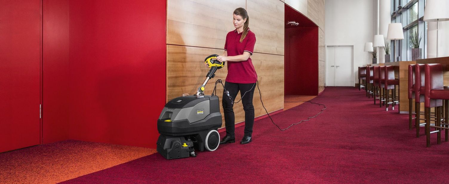 A woman cleans a red carpet with a Kärcher handheld vacuum sweeper