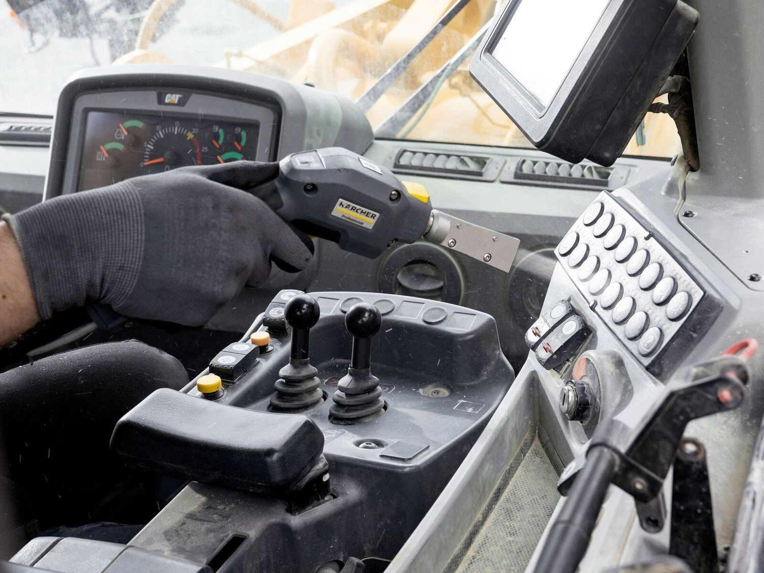 A hand cleans the cockpit of a construction machine with a Kärcher Dry Ice Blaster