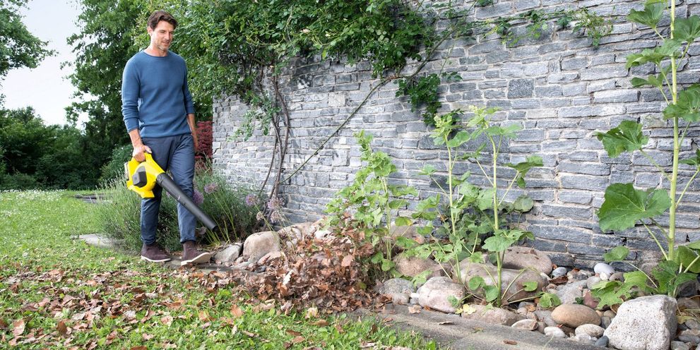 A man removes leaves in the garden with a Kärcher leaf blower