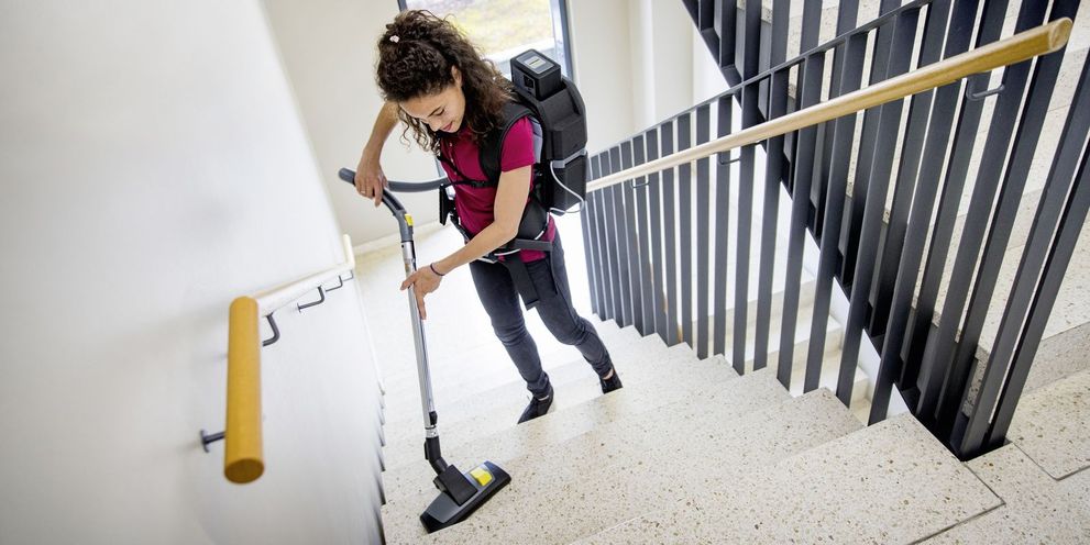 A person cleans a staircase with a battery backpack vacuum cleaner