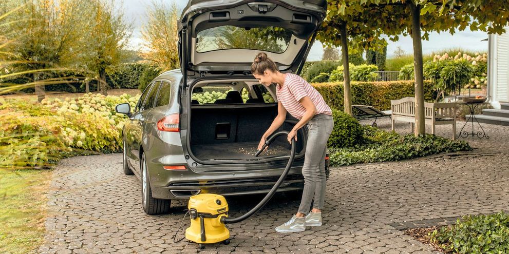 A woman vacuums the boot of the car with Kärcher vacuum cleaner