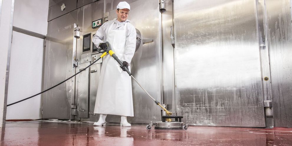 A man in white work clothes mops the floor of a butcher shop using a Kärcher scrubber dryer