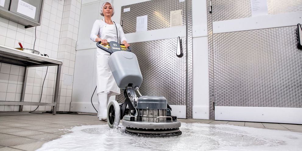 A woman in white work clothes cleans the floor of a butcher shop with a Kärcher single disc machine