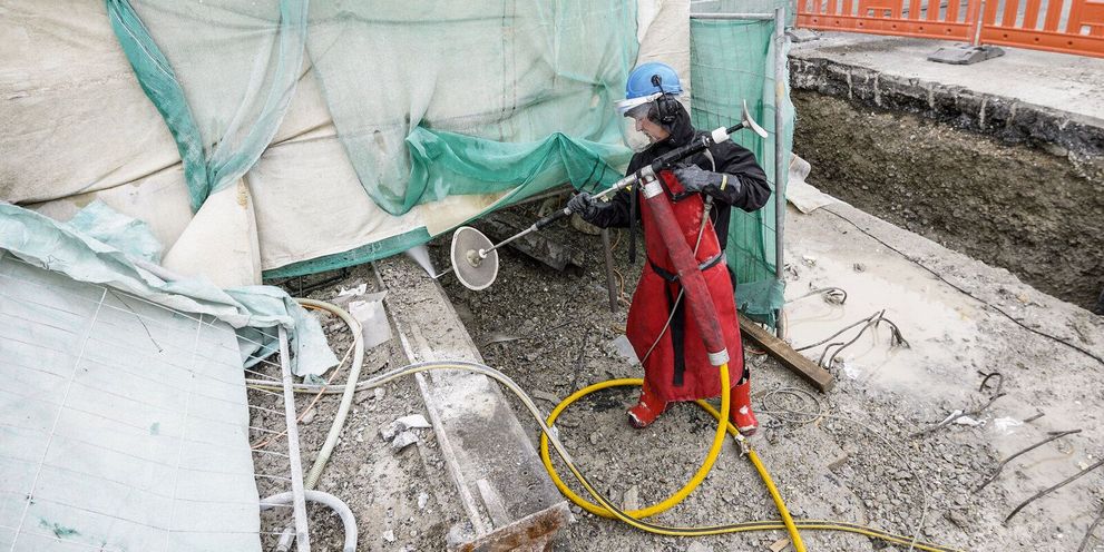A person in a protective suit cleans concrete with an ultra-high-pressure cleaner during bridge repair