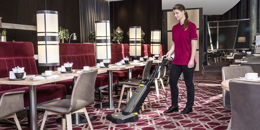 A woman cleans the carpet with a Kärcher brush-type vacuum cleaner