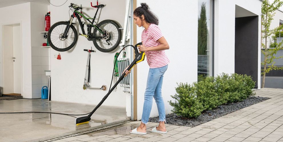 A woman cleans the garage floor with a Kärcher power scrubber