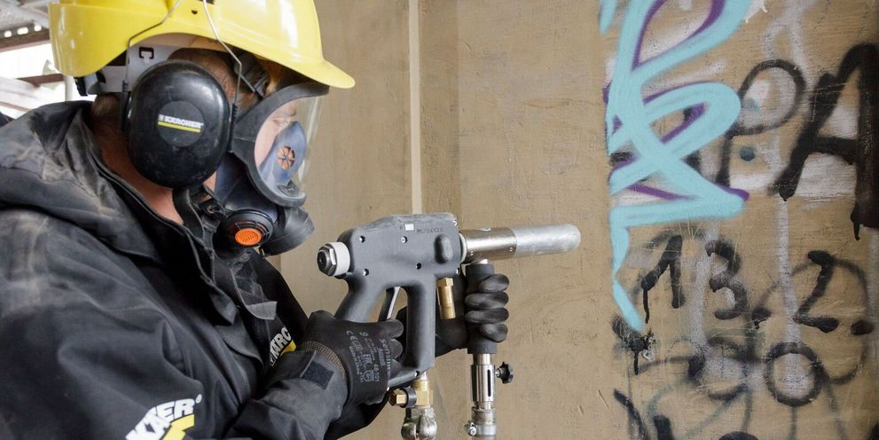 A person removes graffiti from a stone wall