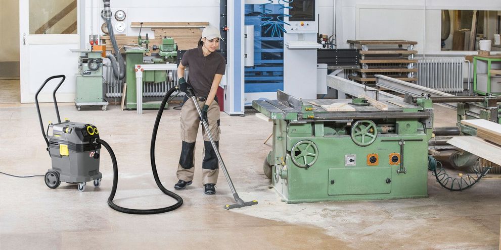 A person cleans the floor in a workshop with a Kärcher Vacuum Cleaner