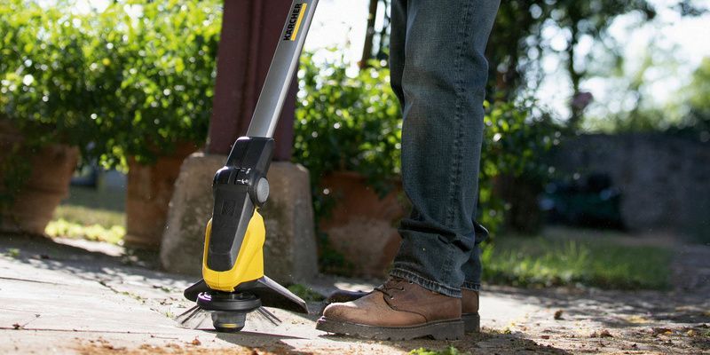 Persoană care îndepărtează buruienile de pe o terasă din piatră cu aparatul de îndepărtat buruieni Kärcher