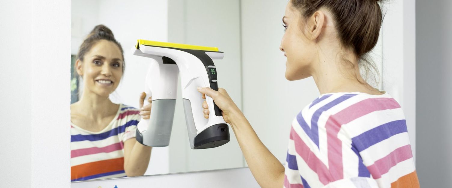 A woman cleaning a mirror with the Kärcher Window Vac