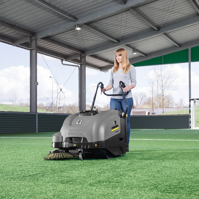 Woman seen cleaning artificial turf using a push vacuum sweeper