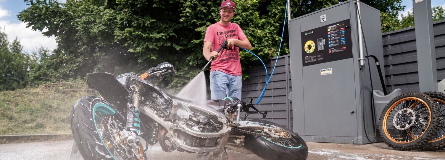 A man cleans his lying-down motorcycle in a Kärcher wash box
