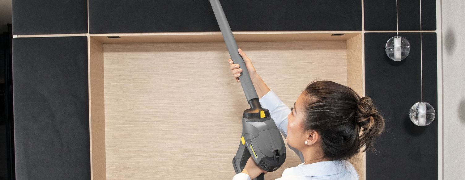 Overhead cleaning A woman uses a Kärcher vacuum cleaner with a telescopic pole to remove dirt from overhead areas