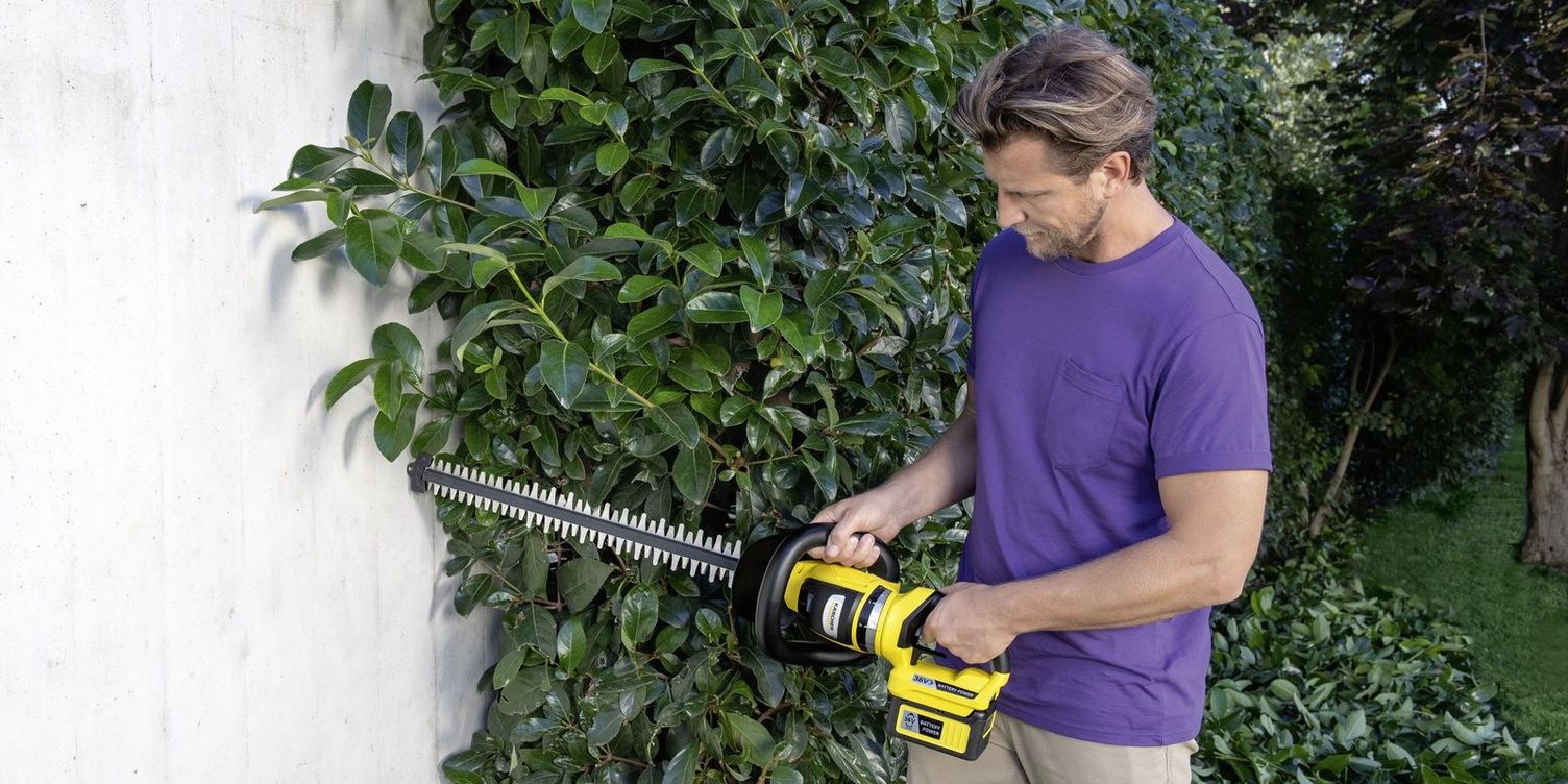 A man trims his hedge near a wall with the Kärcher battery hedge trimmer