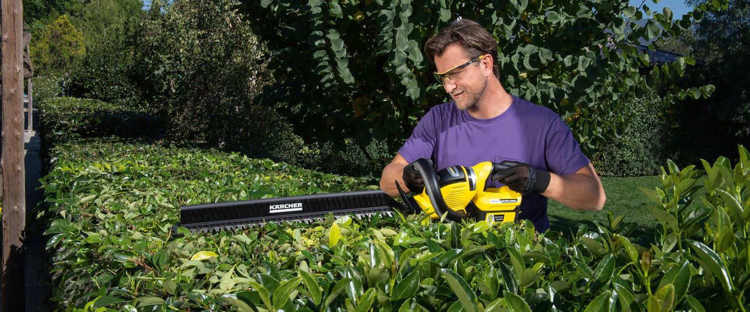 A man uses a Kärcher battery hedge trimmer to cut his hedge from above to a length of