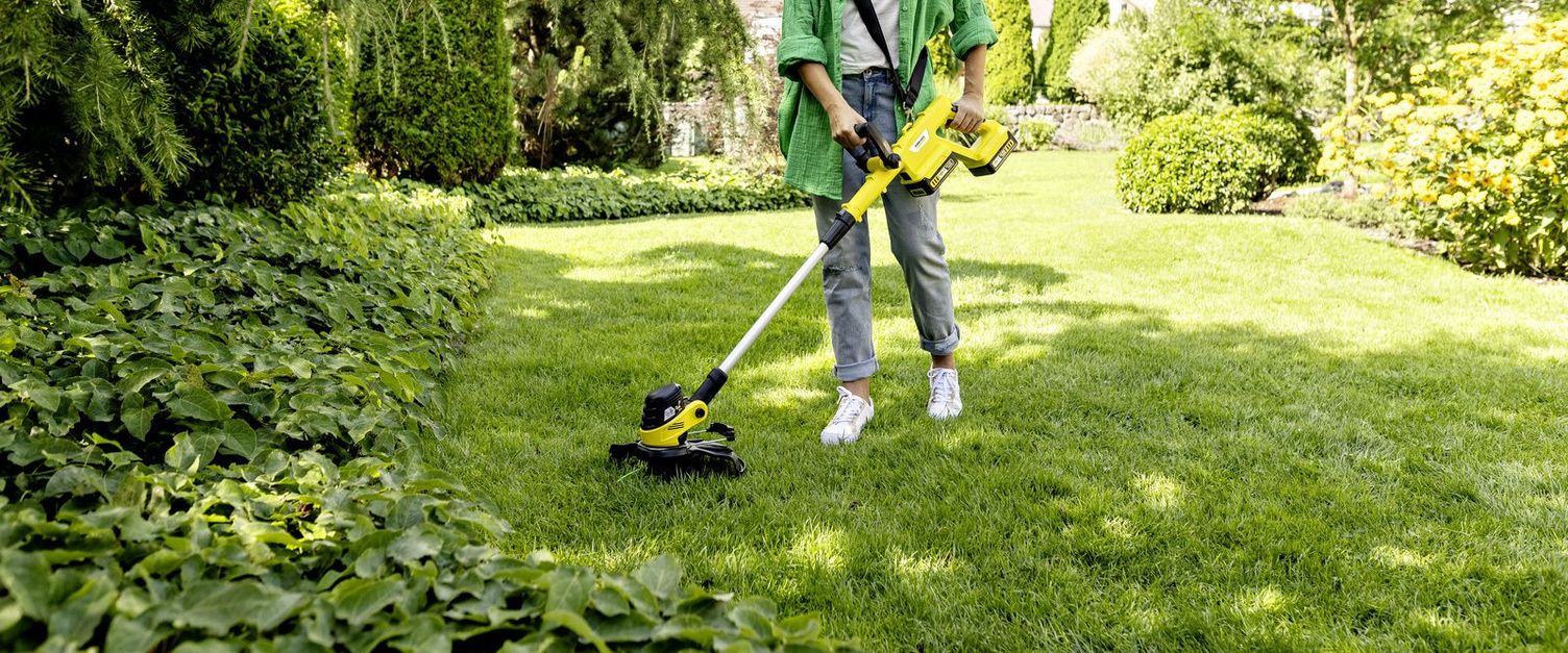A woman uses the Kärcher battery lawn trimmer to trim the lawn under a garden bench