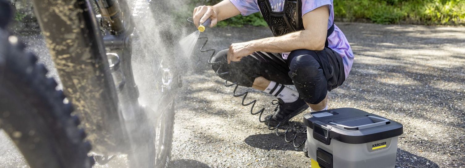 A woman cleans her road bike by a tree with a Kärcher Mobile Outdoor Cleaner