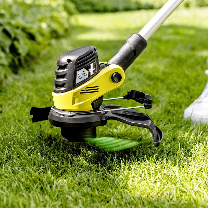 A Kärcher battery-powered lawn trimmer trims the grass near an edge
