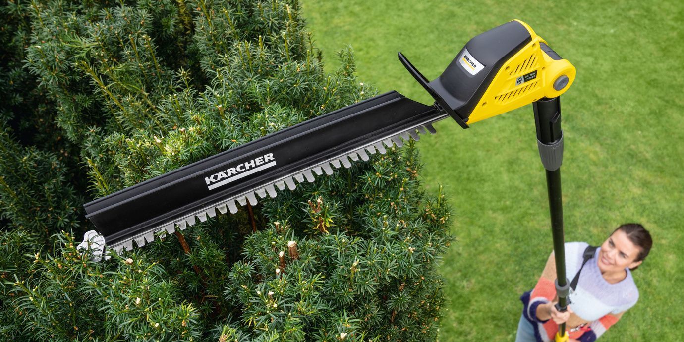 from above: A woman trims her hedge with the help of the Kärcher battery-powered pole hedge trimmer