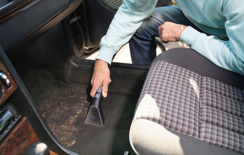 Cleaning car interiour with long, flexible suction hose of spray extraction cleaner